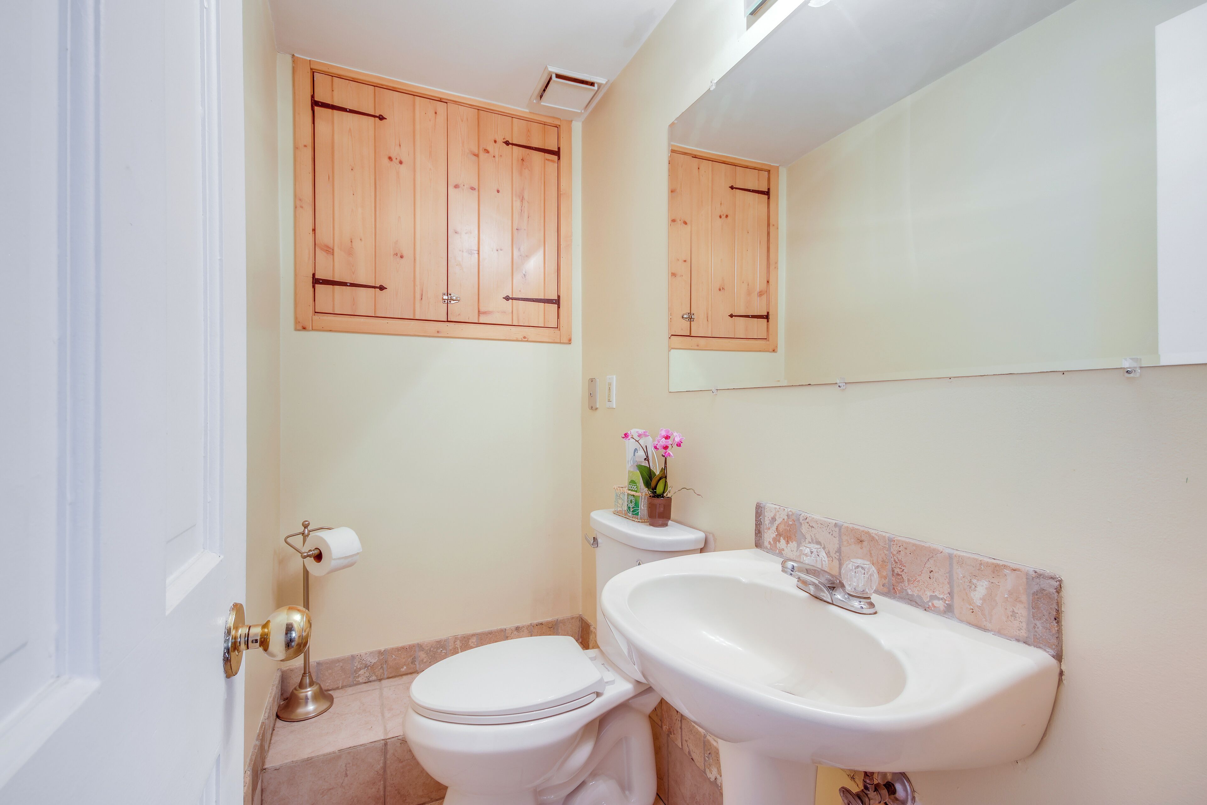 A bathroom with a toilet, sink, wooden cabinets, and a mirror.