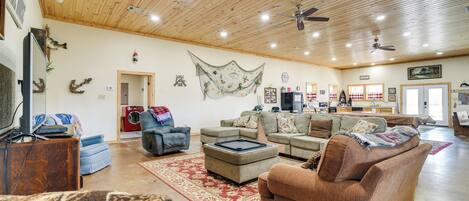 A spacious living room with a high wooden ceiling, multiple sofas, a coffee table, and a television.