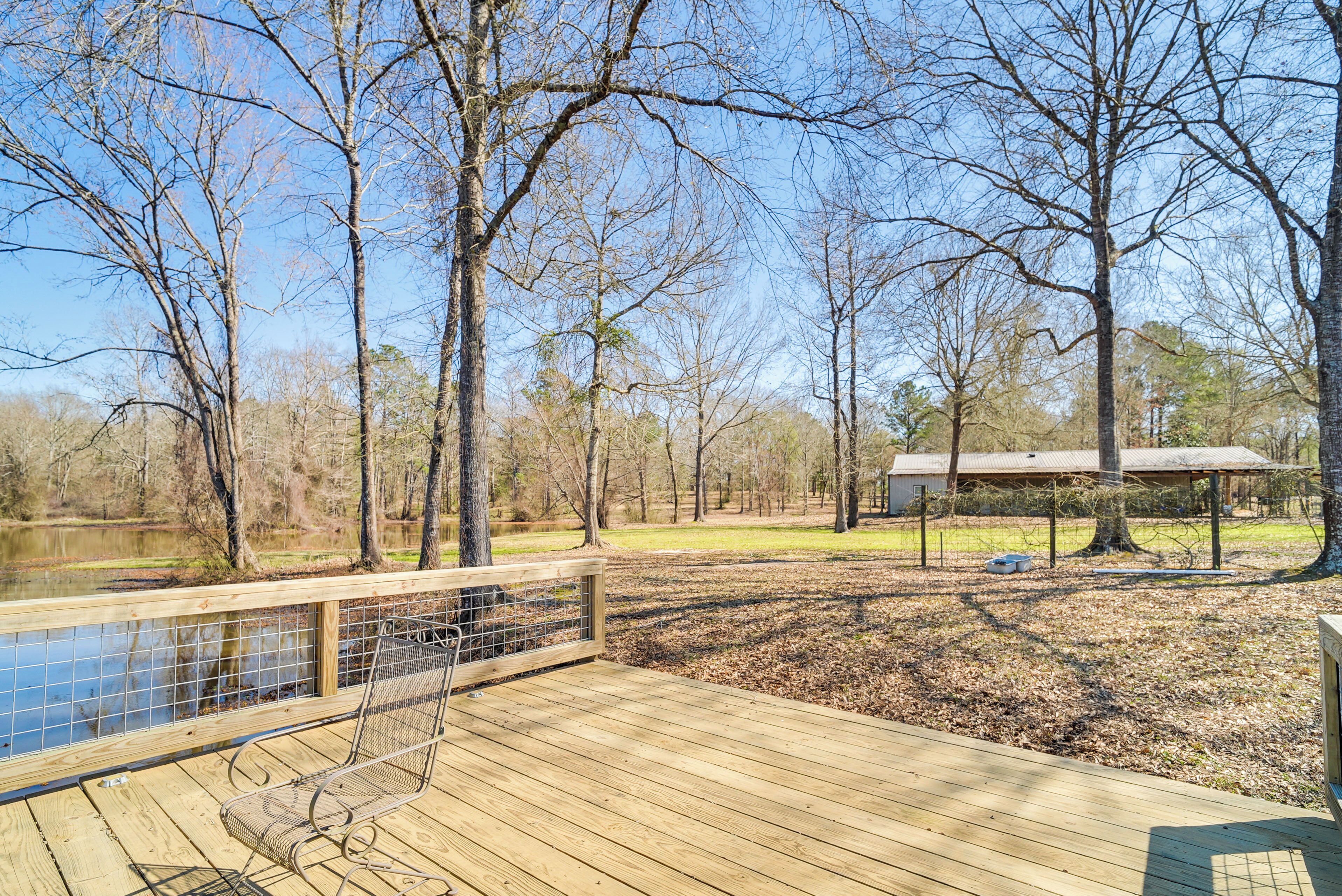 A wooden deck with a metal chair, a small pond, and trees in the background.
