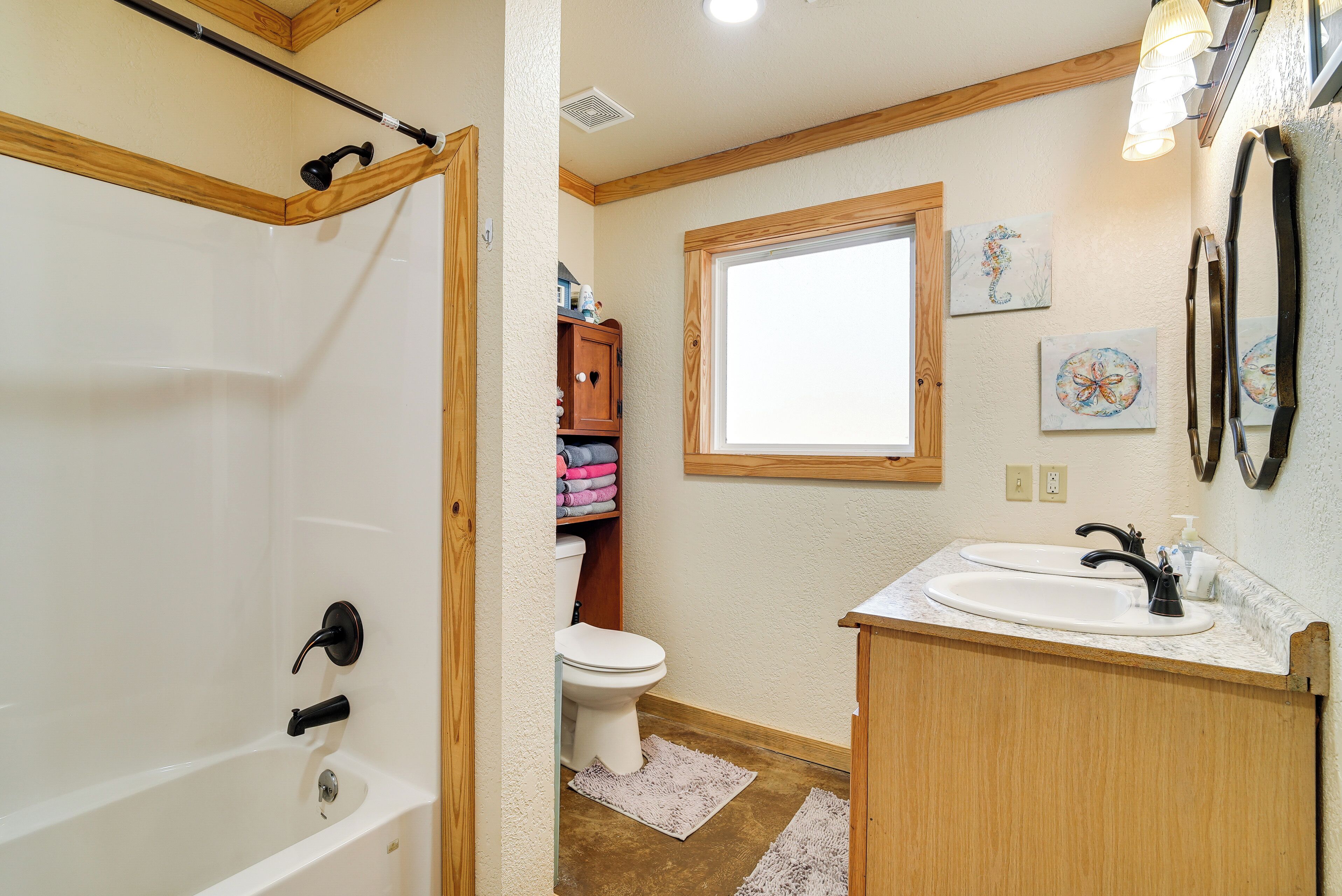A bathroom with a bathtub, toilet, sink, wooden cabinetry, and artwork on the walls.