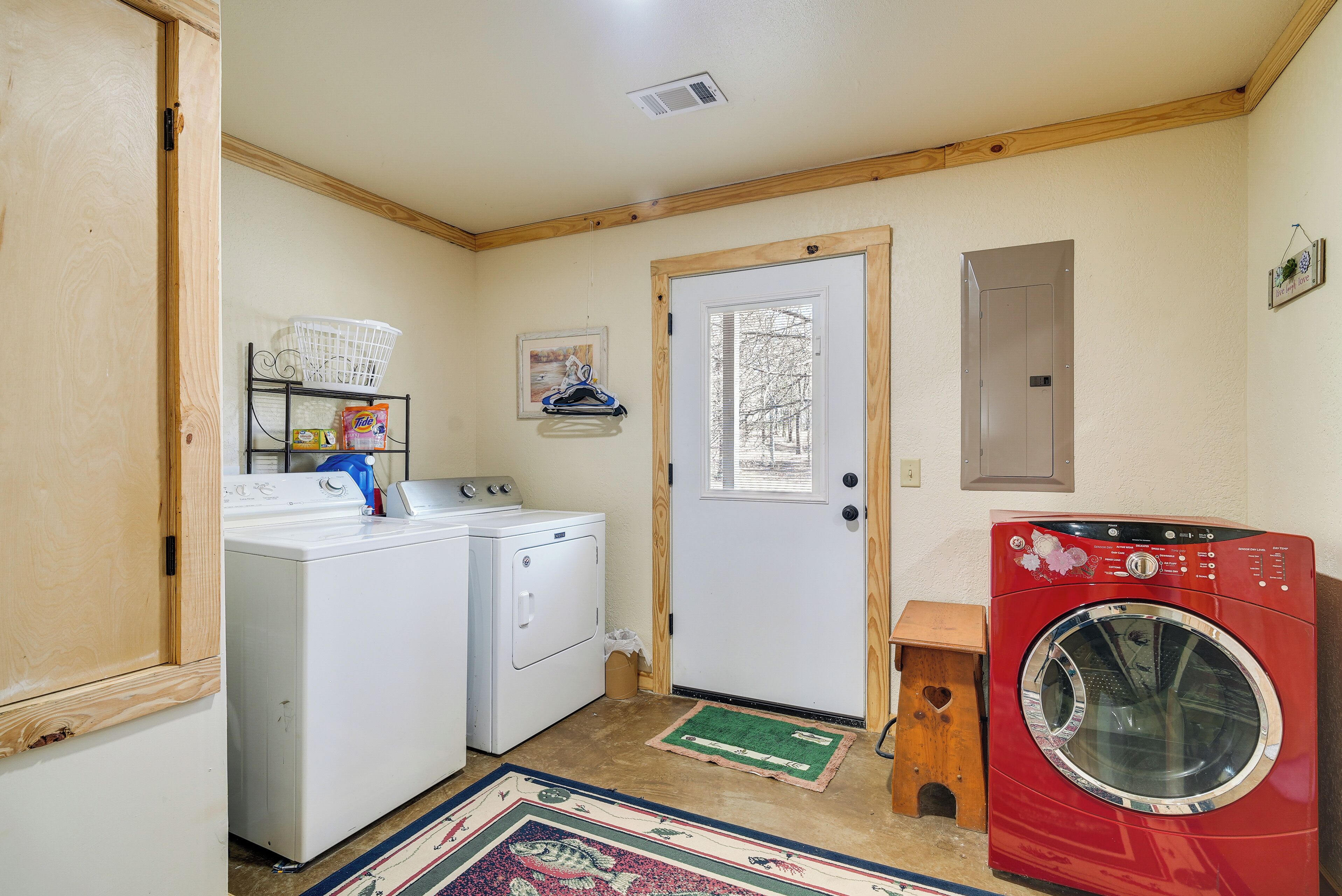 A laundry room with a white and red washer and dryer, wooden cabinets, a small wooden stool, and a green rug.