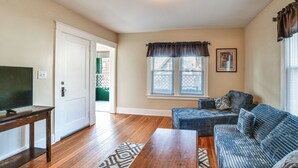 A living room with hardwood floors, a television on a wooden stand, a blue sofa, and a patterned rug. - 1 Mi to Dtwn Binghamton: Apt w/ Covered Balcony! (Binghamton)