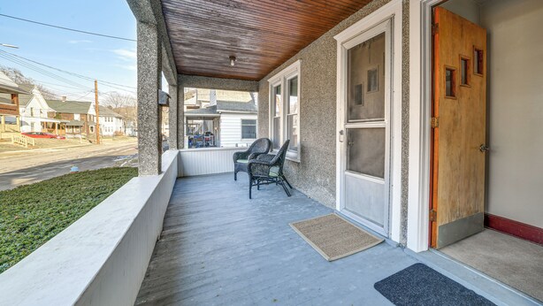 A covered porch with two wicker chairs, a wooden door, and a view of the street. - 1 Mi to Dtwn Binghamton: Apt w/ Covered Balcony! (Binghamton)