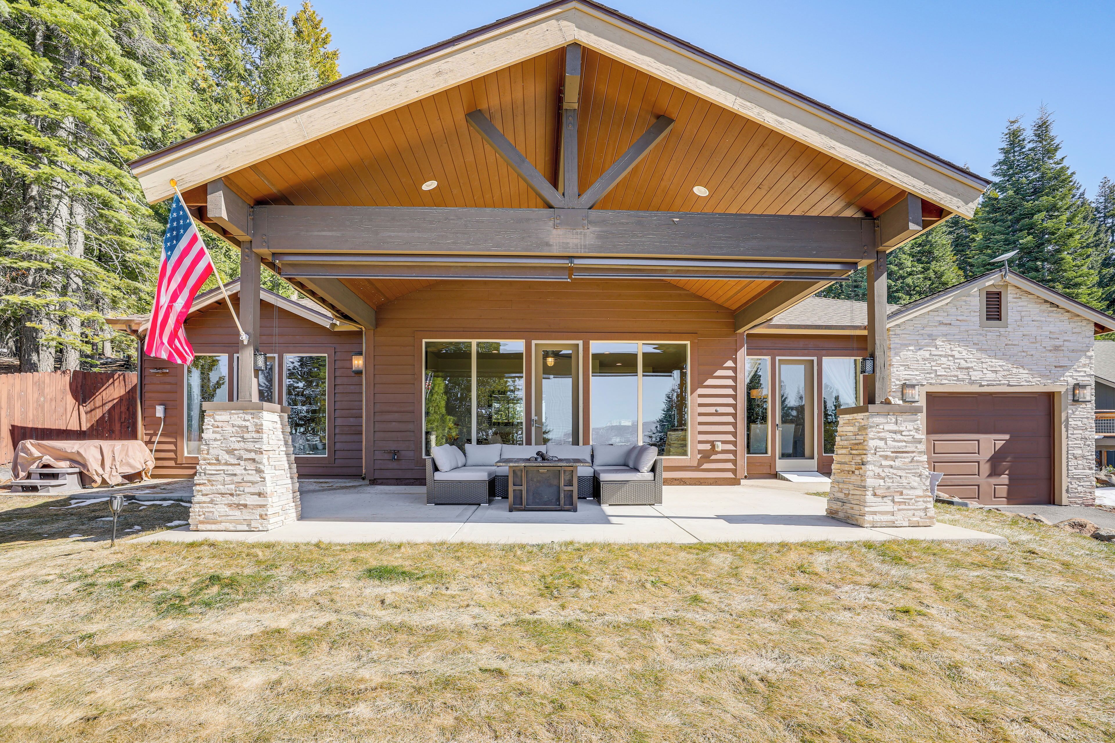 A covered patio area with a stone pillar, a flag, and a stone building in the background.