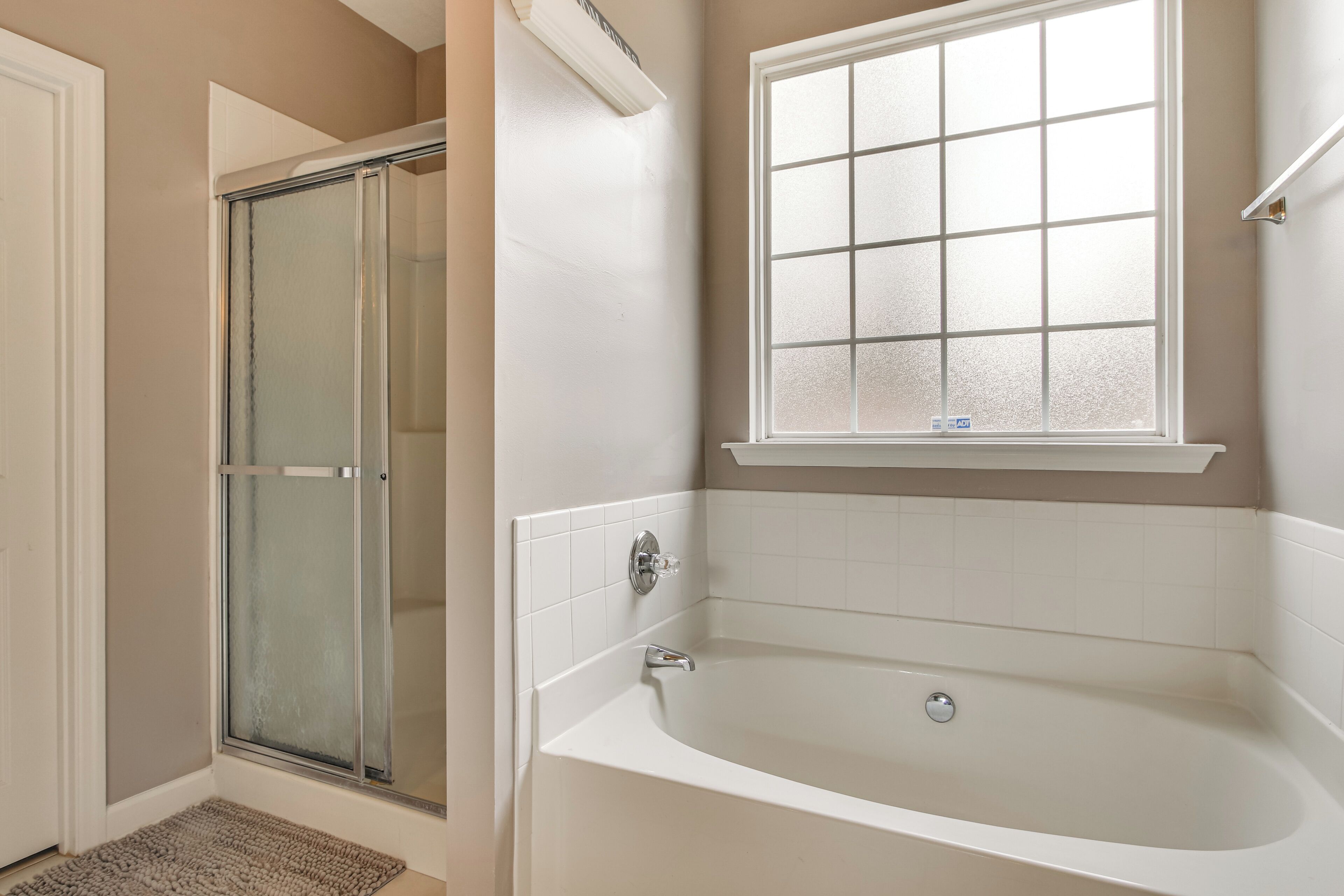 A bathroom with a glass shower enclosure, a bathtub, and a window above the tub.