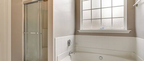 A bathroom with a glass shower enclosure, a bathtub, and a window above the tub.