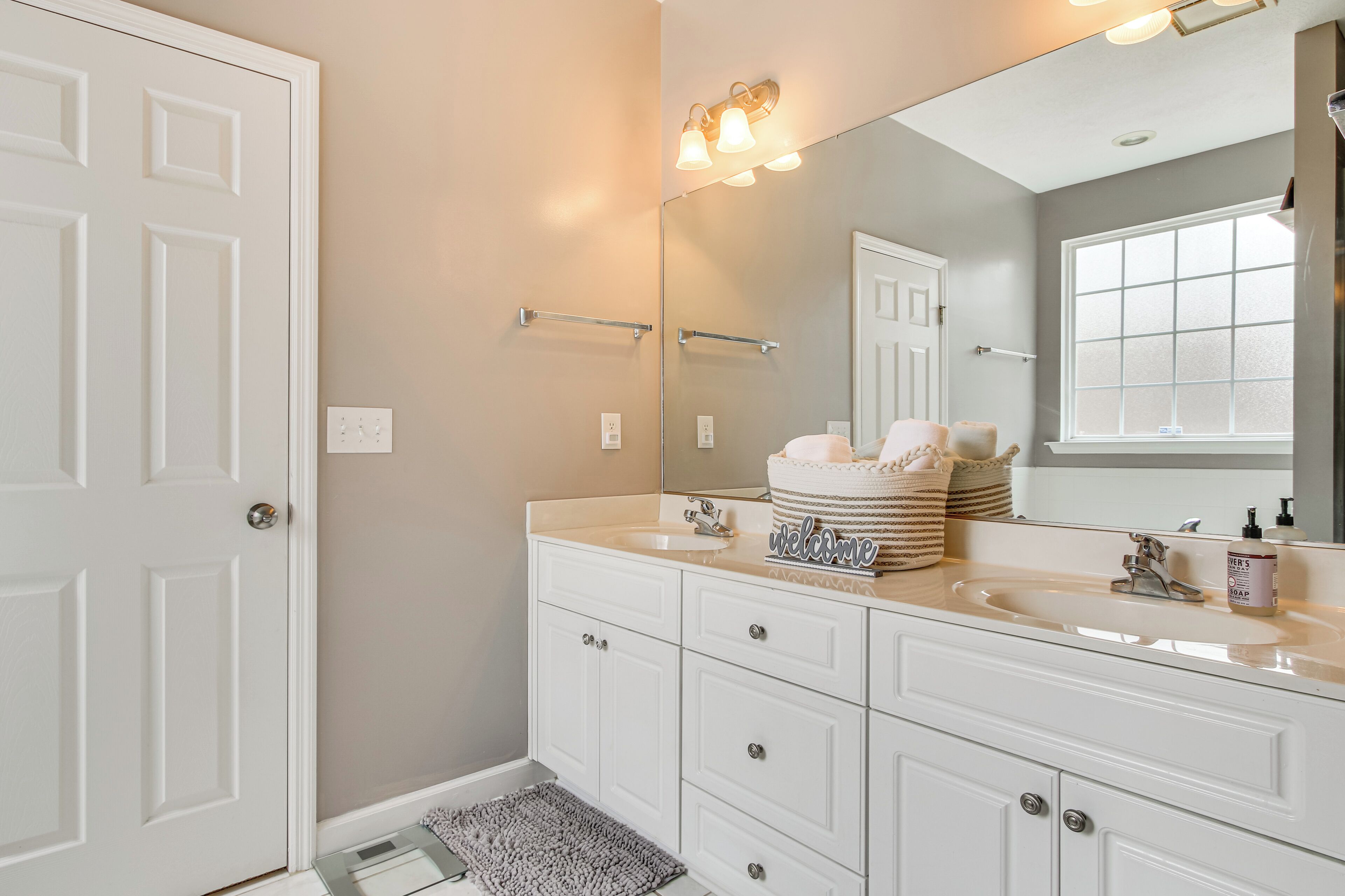A bathroom with a white vanity, a large mirror, and a window.