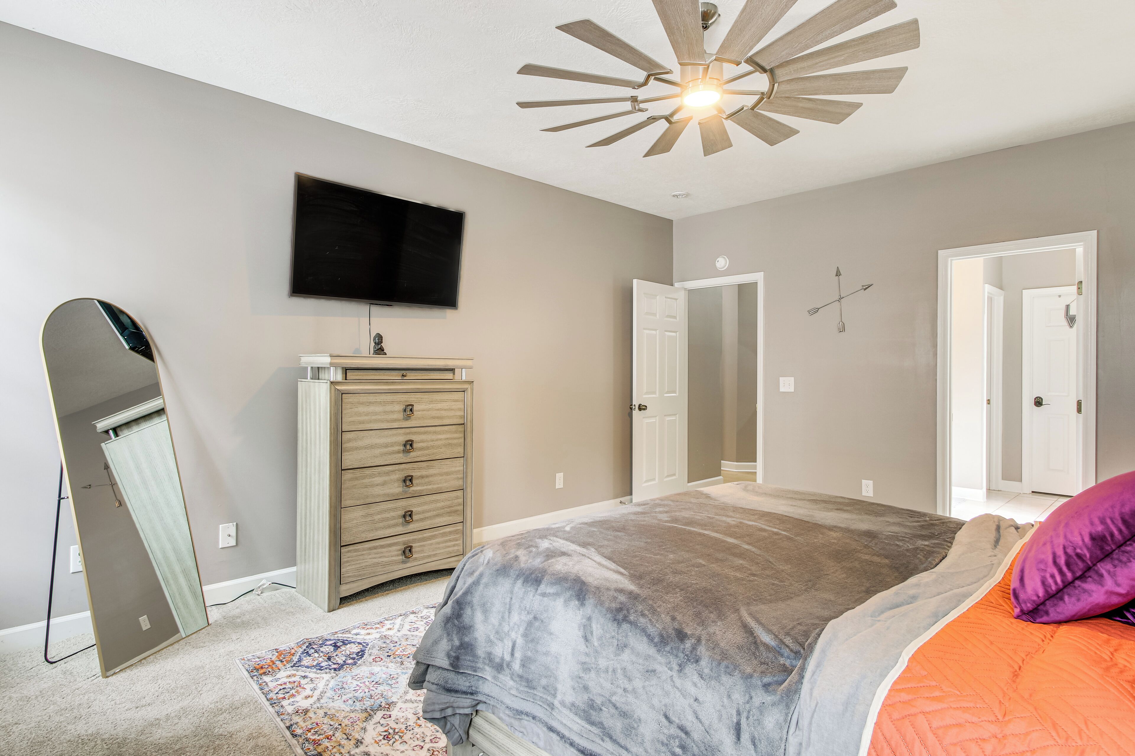 A bedroom with a bed, dresser, mirror, television, and a ceiling fan.