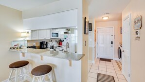 Una cocina moderna con gabinetes blancos, encimera de granito y dos taburetes de bar.