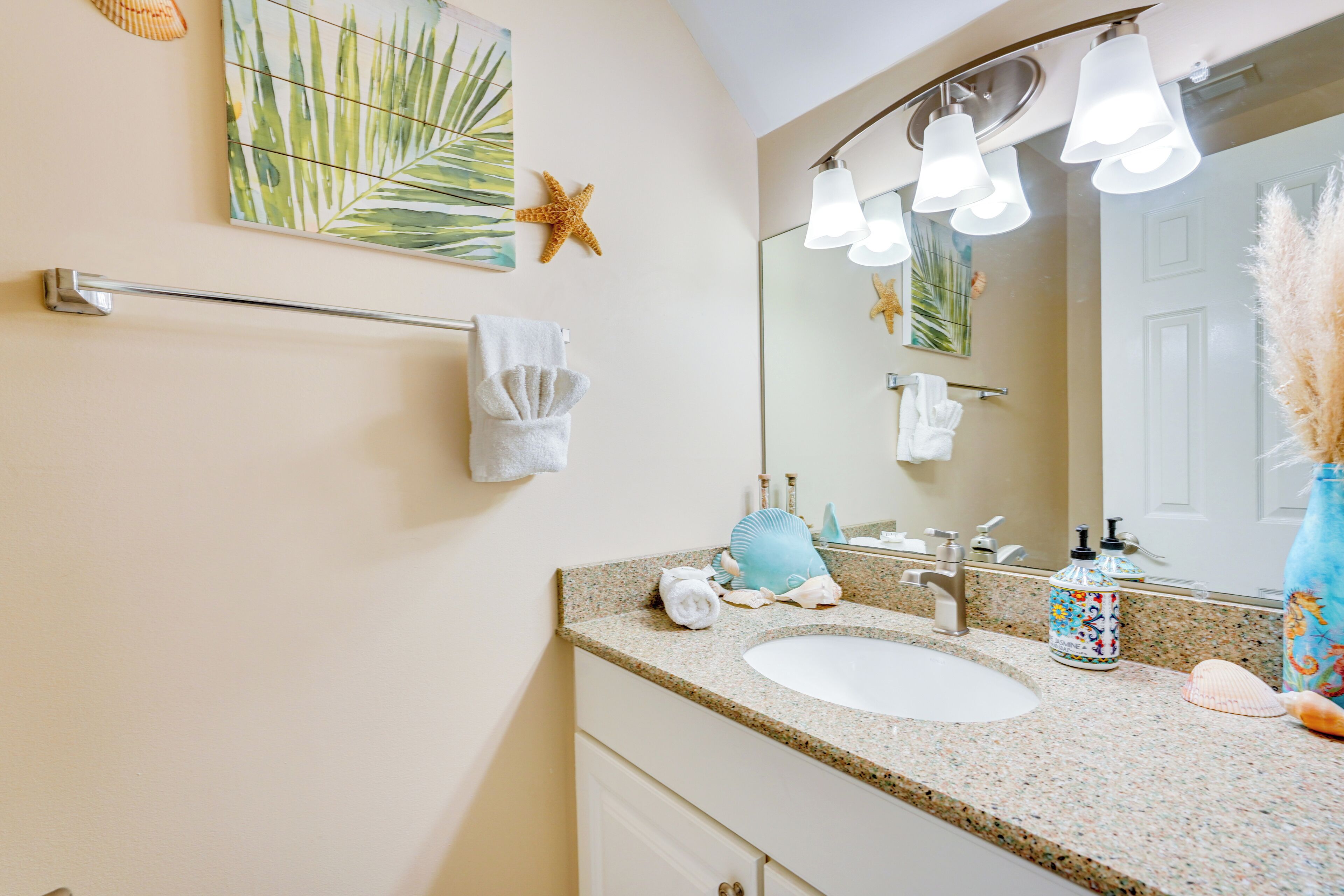 A bathroom with a granite countertop, two sinks, a towel rack, a large mirror, and decorative items like a starfish and a seashell.