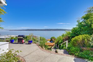 Eine Terrasse mit Grill, blauen Müllbehältern und Blick aufs Wasser.