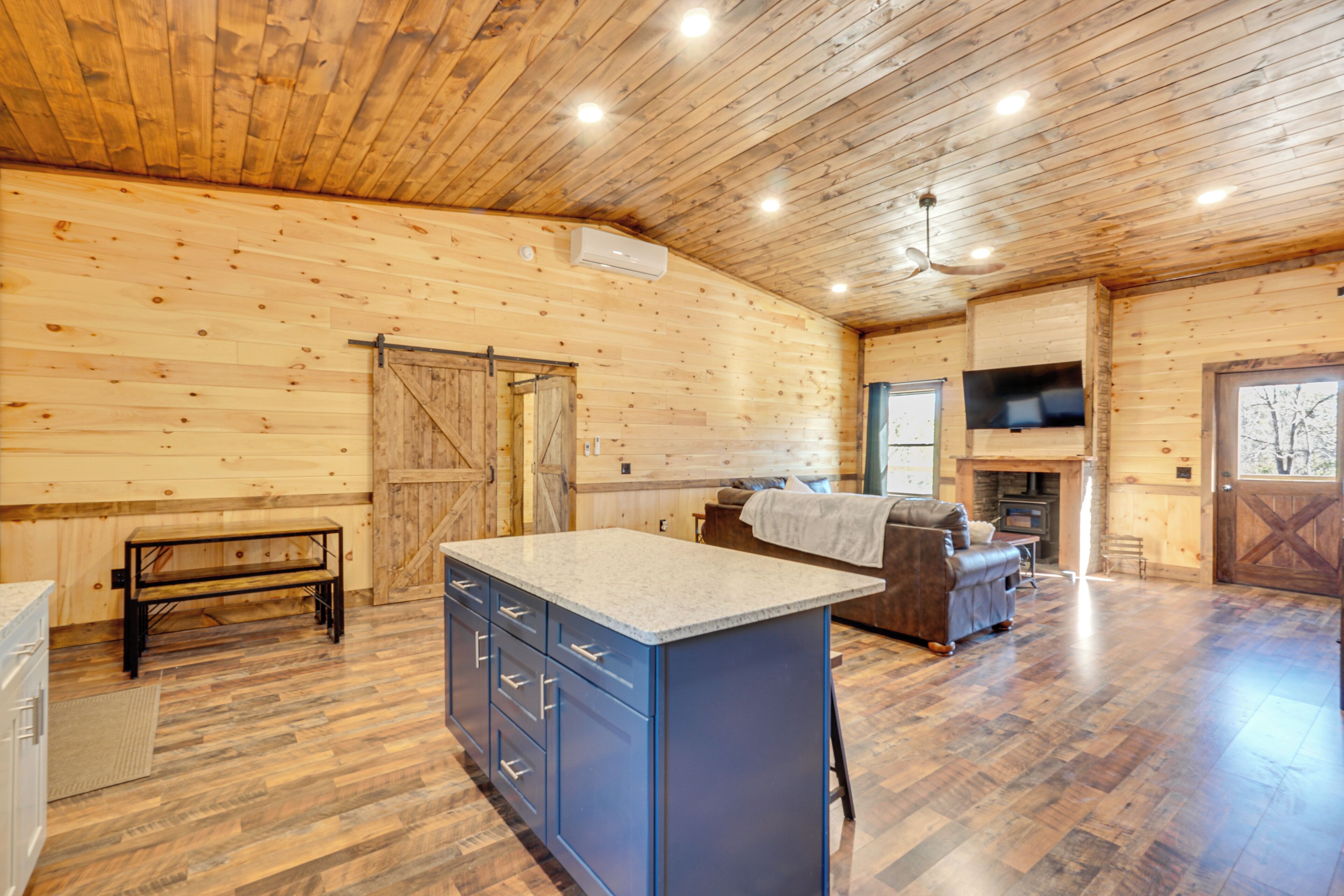 A spacious room with wooden walls, a large island with drawers, a sofa, and a fireplace.