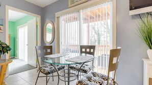 A dining area with a glass-top table, patterned chairs, and a view through a window with blinds. - Walk to Eastern Point Beach: Apt w/ Water View! (Groton)