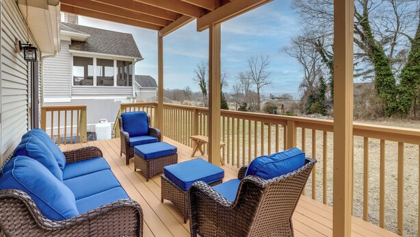 A covered outdoor deck with wicker furniture and blue cushions, overlooking a residential area. - Walk to Eastern Point Beach: Apt w/ Water View! (Groton)