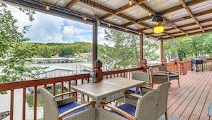 A covered outdoor deck with wicker furniture and a view of a lake and buildings.