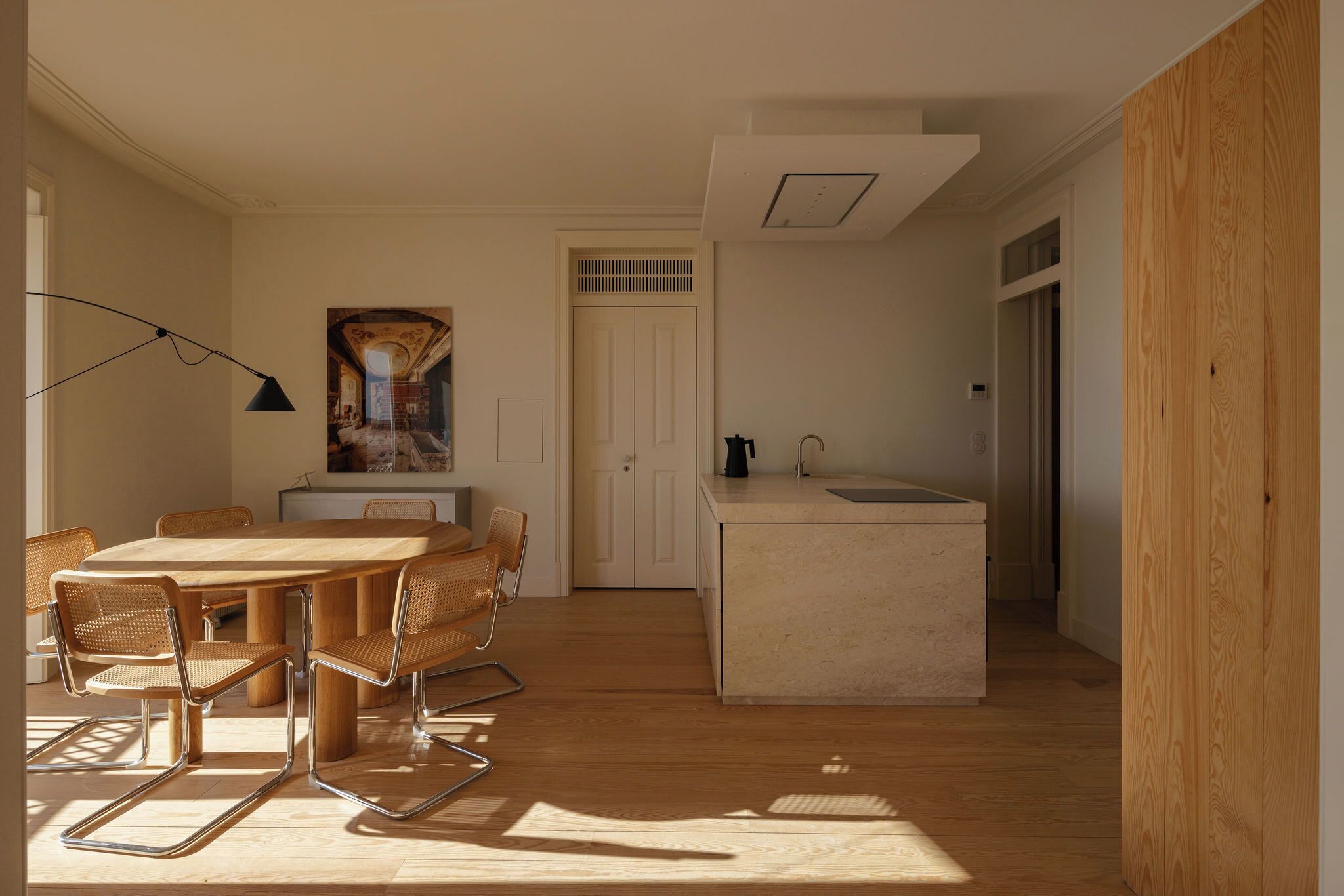 Een moderne keuken met een centraal eiland, een eethoek met een ronde tafel en stoelen, en uitzicht op een deur die leidt naar een andere kamer.