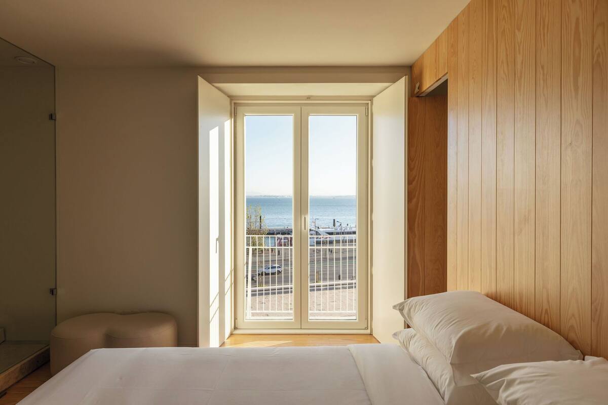 A bedroom with a large window, a bed, and a wooden wall.