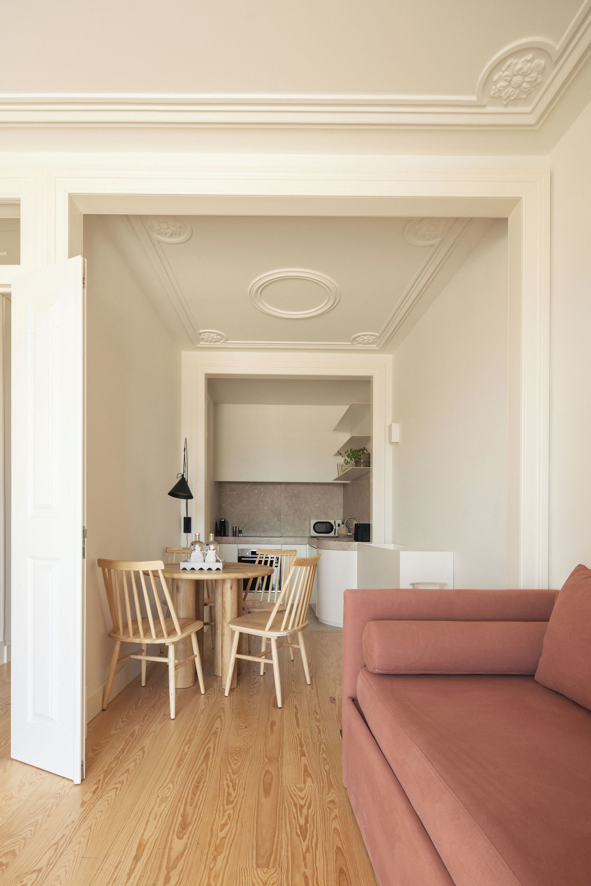 Un salon moderne avec un plancher en bois, un canapé rose et un coin repas comprenant des chaises en bois et une petite table.