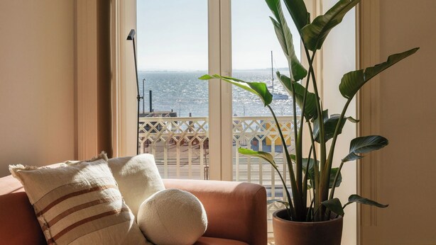 A room with a sofa, a potted plant, and a view of the city through a large window. - LIOZ Lisboa (Lisbon)