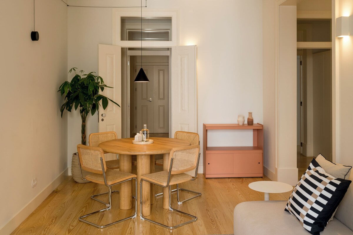 Et spiseområde med et træbord, fire stole, en potteplante og et pink skab.