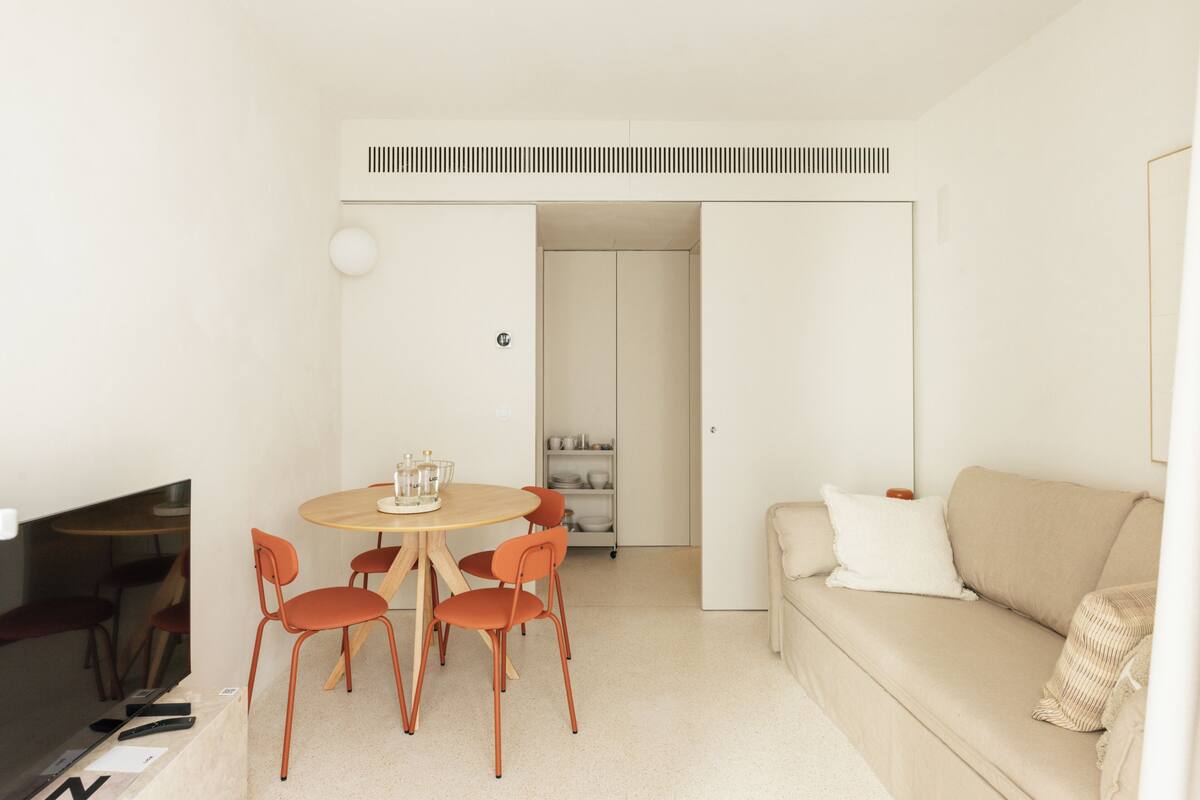 A modern living room with a round dining table, four chairs, a sofa, and a television.