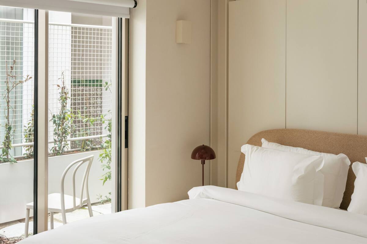 A modern hotel room with a bed, a desk, and a balcony with plants.