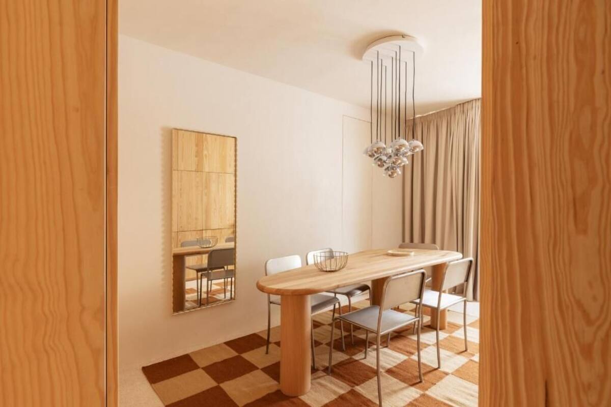 A modern dining area with a wooden table, white chairs, a decorative light fixture, and a checkered floor.