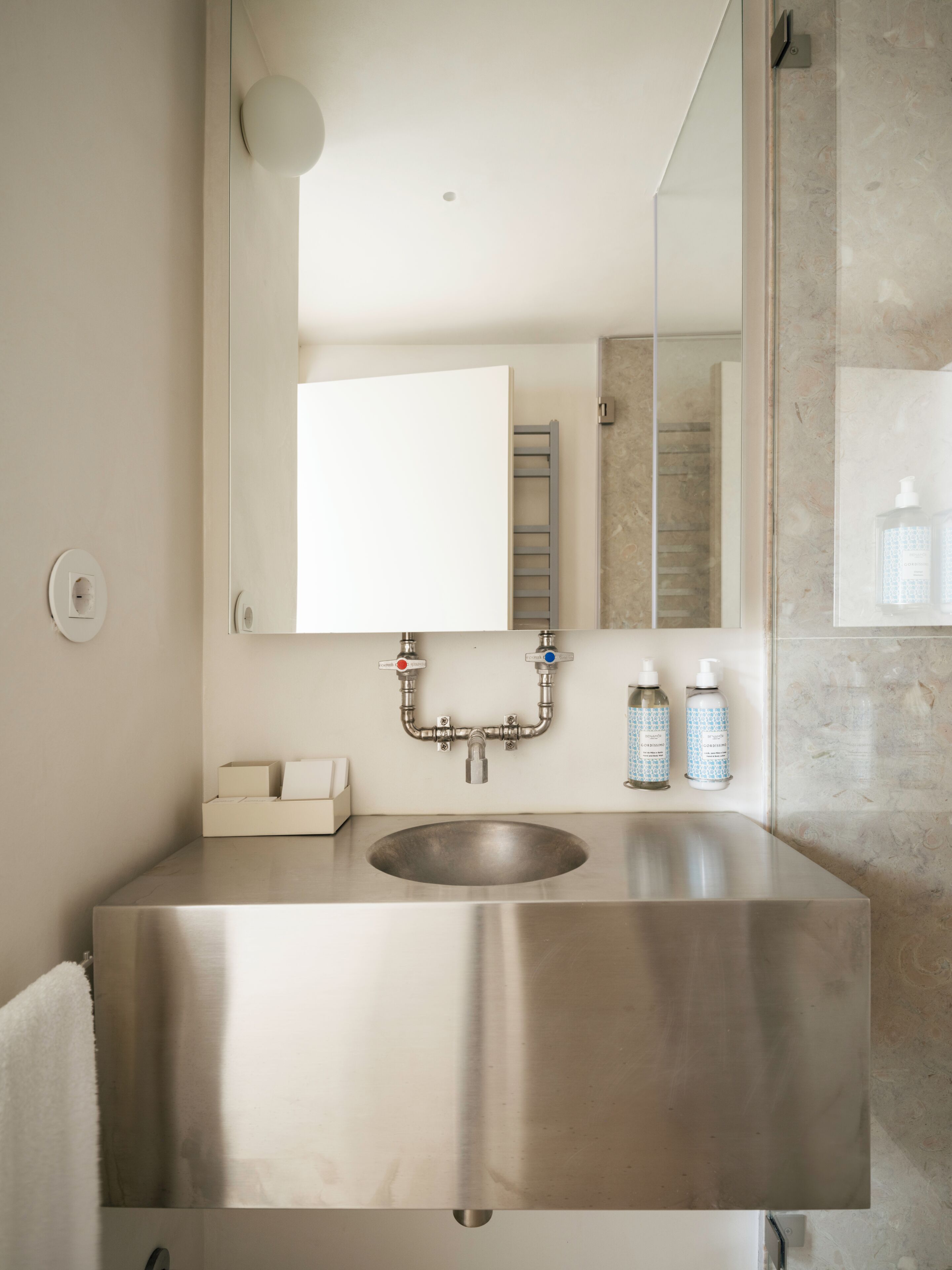 A modern bathroom with a stainless steel sink, a mirror, and a towel rack.