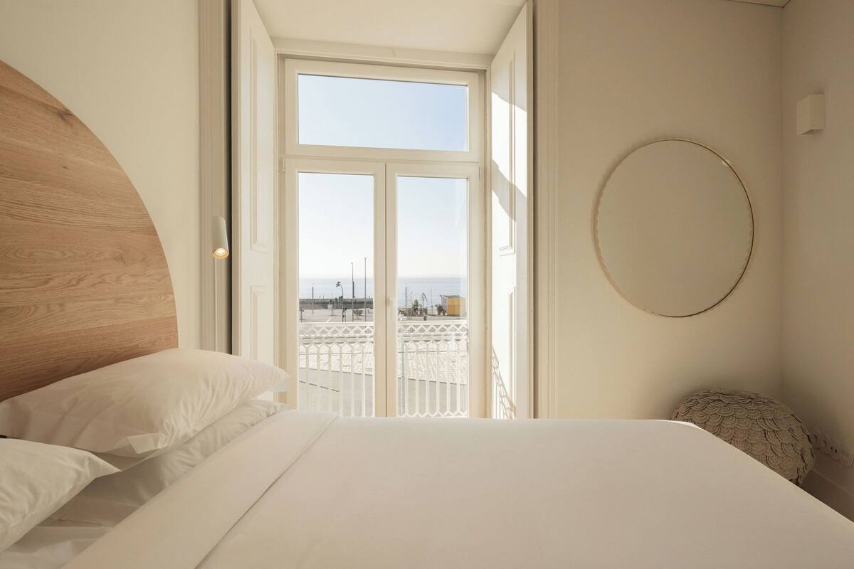 A bedroom with a large bed, a wooden headboard, a circular wall decoration, and a view of the sea through a window.