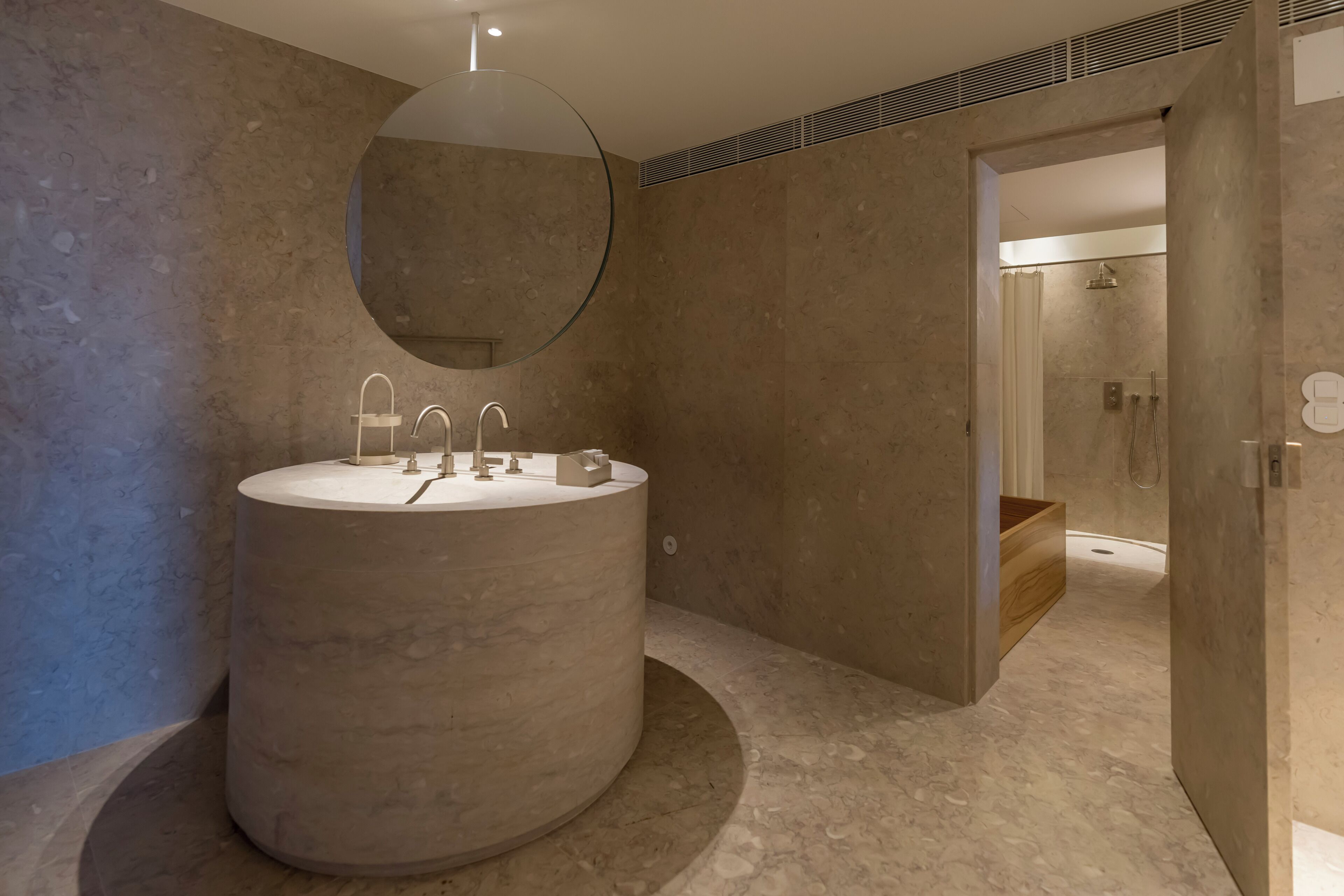 A modern bathroom with a large circular sink, a round mirror, and a shower area.