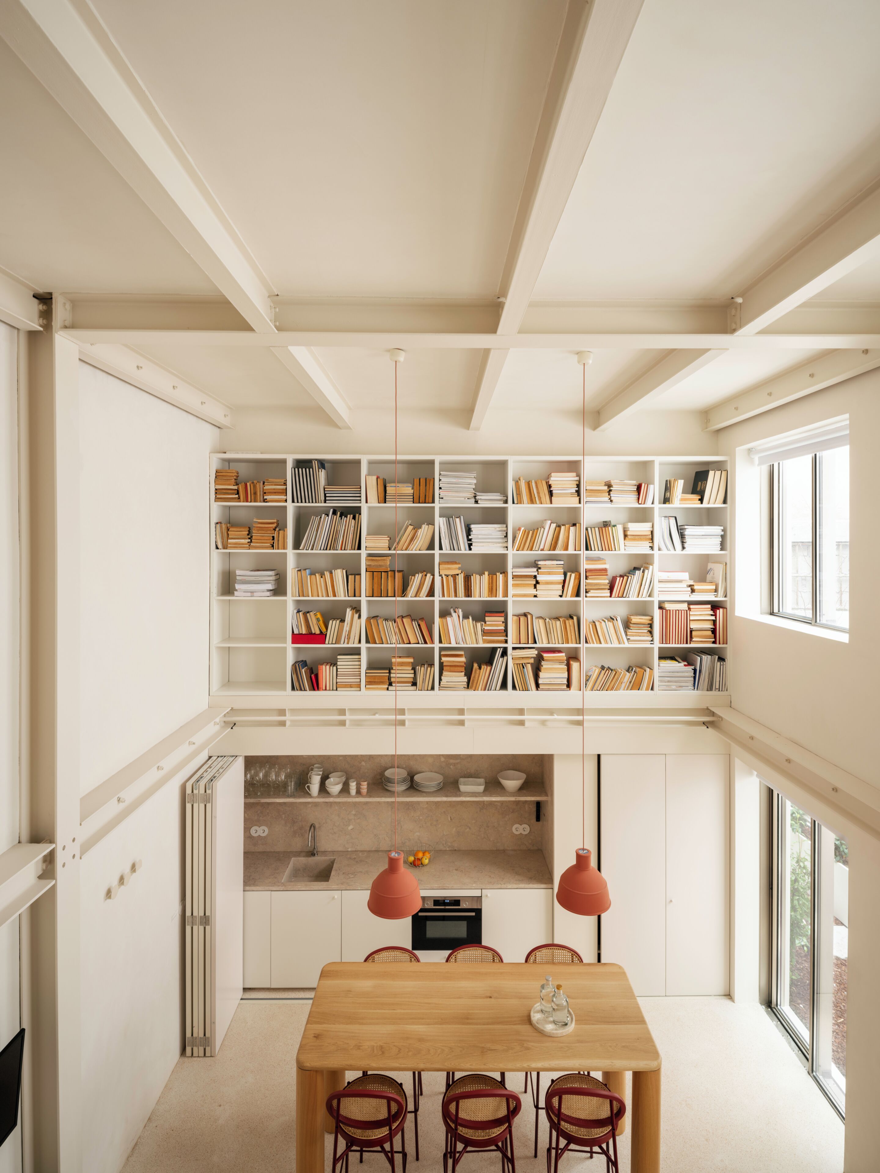 Un intérieur moderne avec une table en bois au centre, une bibliothèque et un coin cuisine.