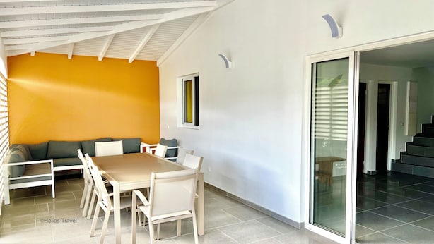 Un comedor moderno con una gran mesa y sillas, un sofá, y una pared de acento naranja brillante.