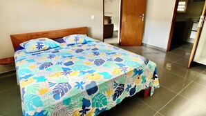 Una cama con cubrecama floral en una habitación con puerta de madera y suelo de baldosas.