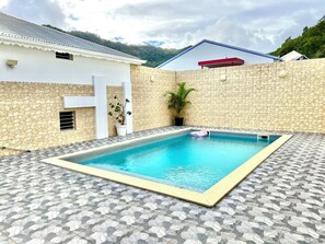Una piscina con una pared de piedra y un edificio blanco con techo rojo.