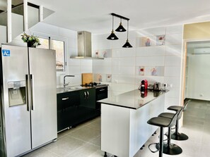 A modern kitchen with a stainless steel refrigerator, a built-in oven, a sink, and a bar area with stools.