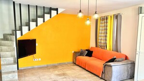 Un salon avec un canapé, un téléviseur à écran plat, un escalier et un mur jaune.