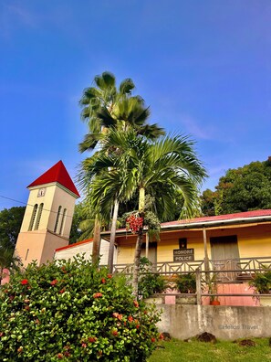Un edificio con una torre de reloj, un cartel que dice "Honeymoon Police" y una palmera con flores rojas.