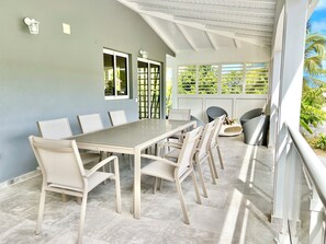 Ein Essbereich mit einem langen Tisch und Stühlen, ein Balkon mit Geländer sowie Blick ins Grüne.