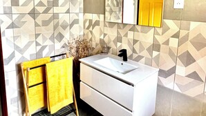 A bathroom with a white vanity, a mirror, and a geometric patterned wall. - Zandoli Apartment. Bas Vent Estate. (Deshaies)