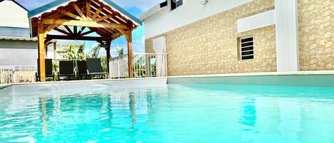 A swimming pool with a wooden pergola and a stone wall.