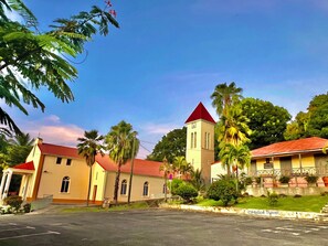 A church with a red roof and a clock tower, surrounded by palm trees and a clear sky.