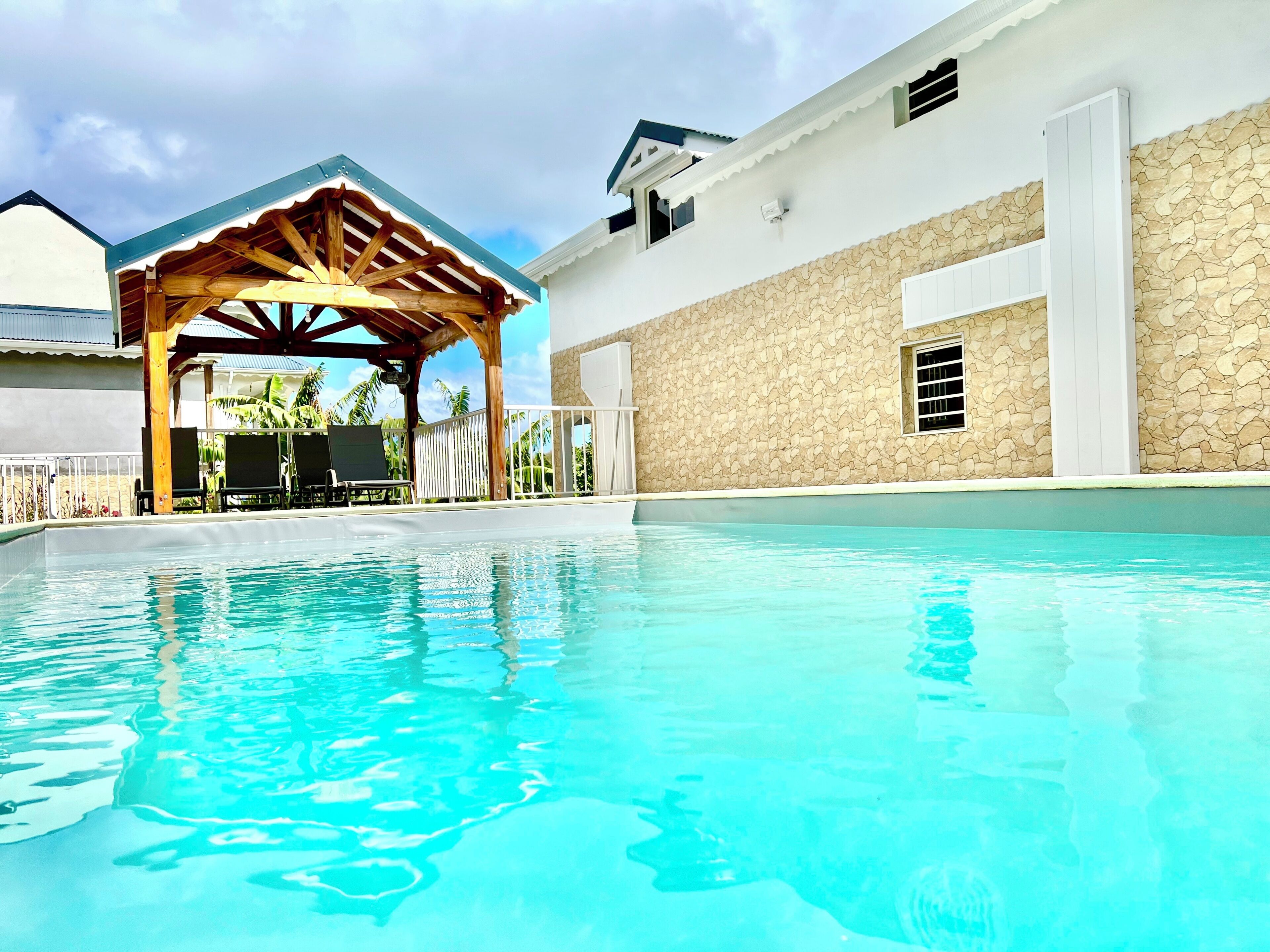 A swimming pool with a wooden pergola and a stone wall.