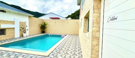 Una piscina con un muro de piedra y una puerta de garaje con la etiqueta 'Colibri'.