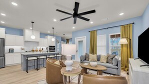 A modern kitchen with white cabinets, a central island, and a dining area with a round table and chairs. - The Bella Muse - 3-Bedroom House W/ Hot Tub close to Bike Trails (Bella Vista)