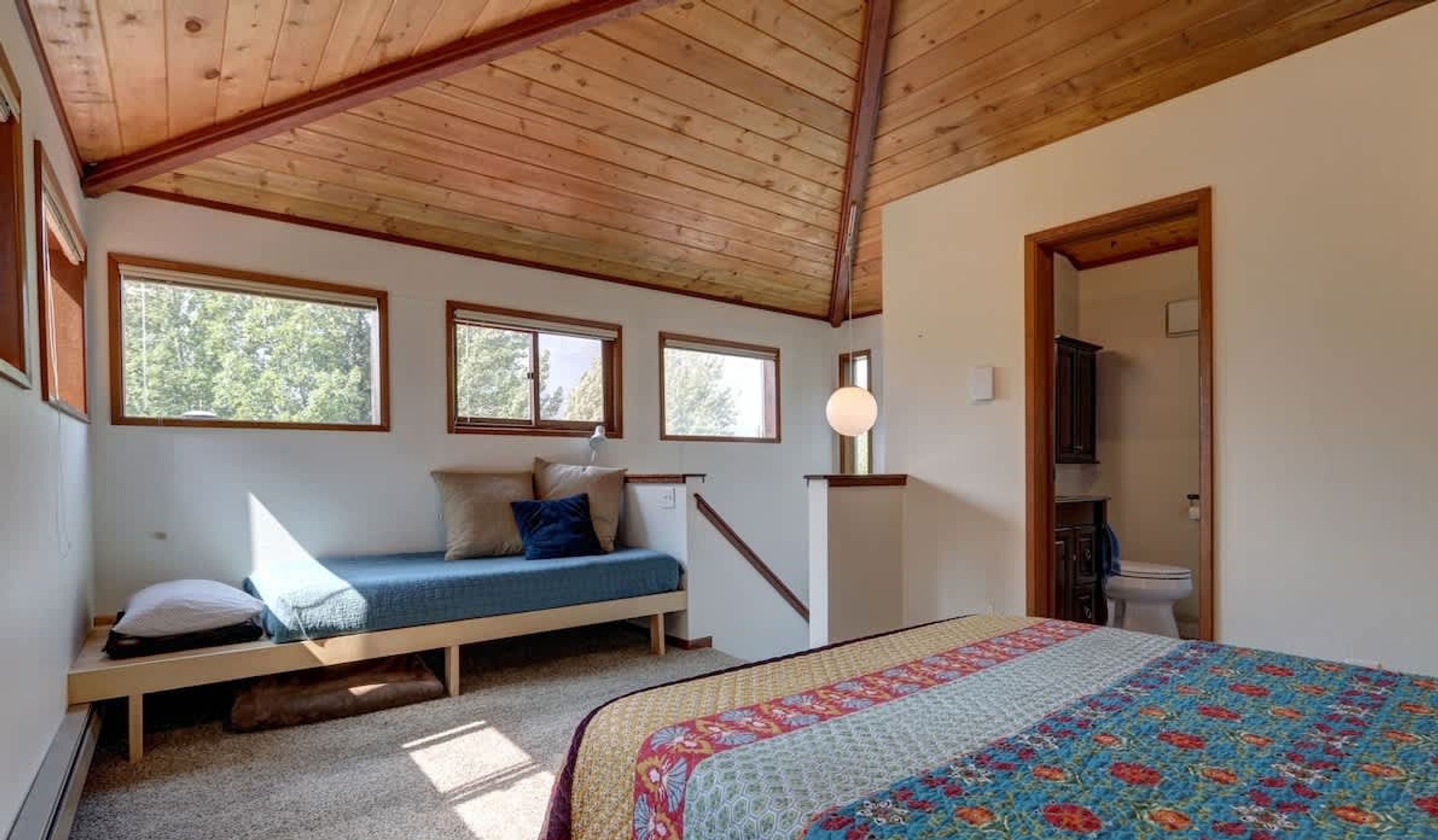 Une chambre avec un plafond en bois, un lit avec un matelas bleu, une table de chevet et une fenêtre.