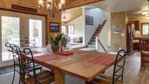 A wooden dining table with chairs, a chandelier, and a staircase leading to another room.