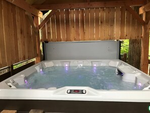 A hot tub with a control panel, surrounded by wooden walls and a view of greenery. - Slopes Spokes Alaska Large HOT TUB (Girdwood)