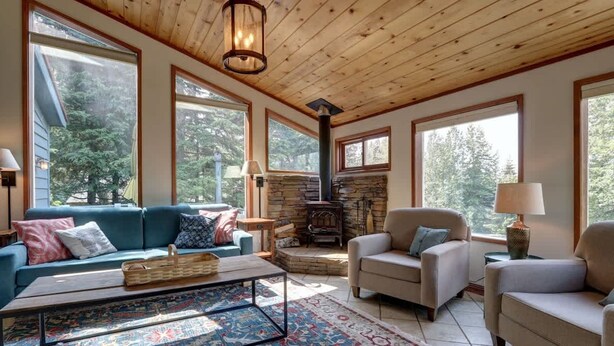 A cozy living room with a stone fireplace, large windows, and a wooden ceiling.