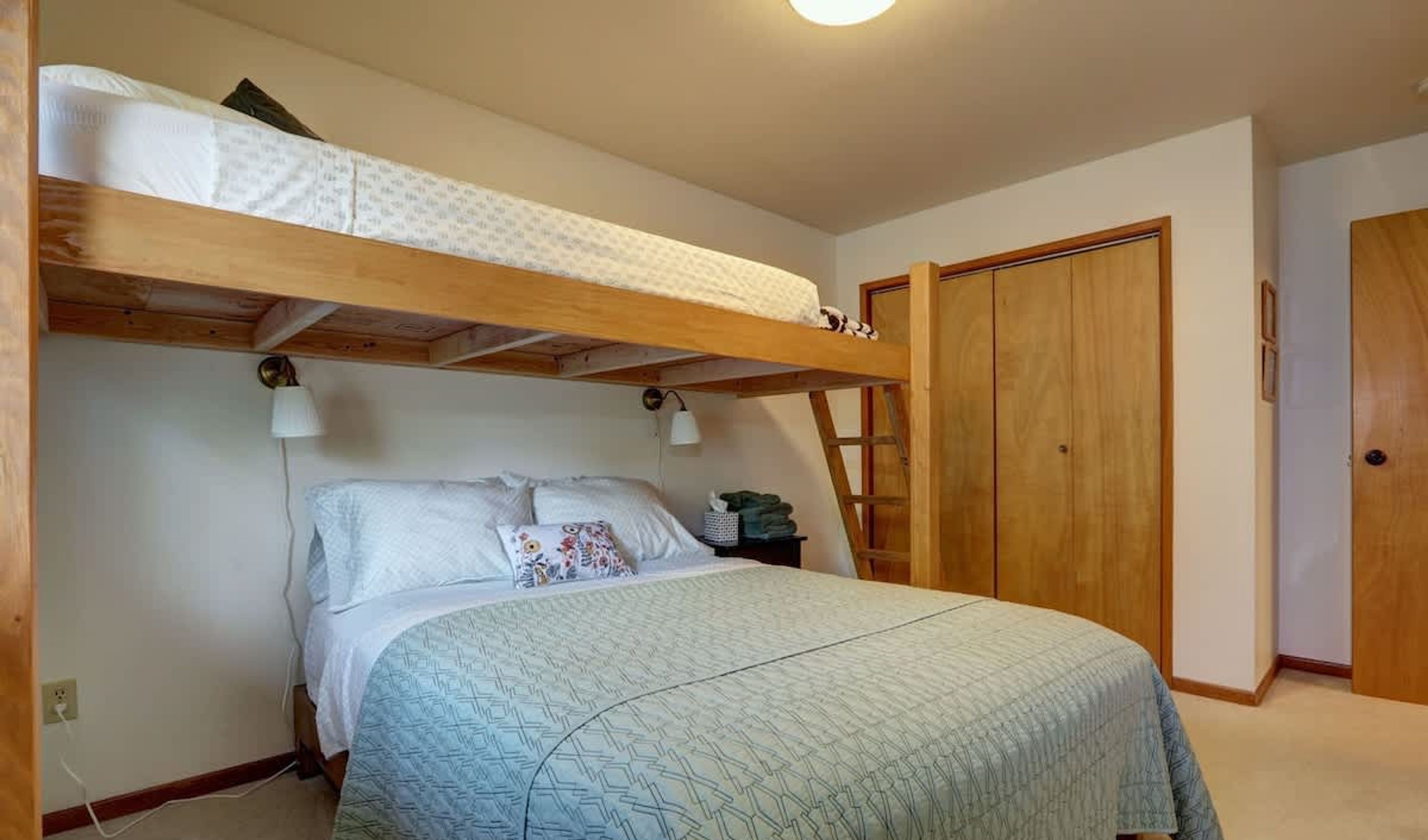A bedroom with a bunk bed, a single bed, a nightstand, a lamp, and a wardrobe.