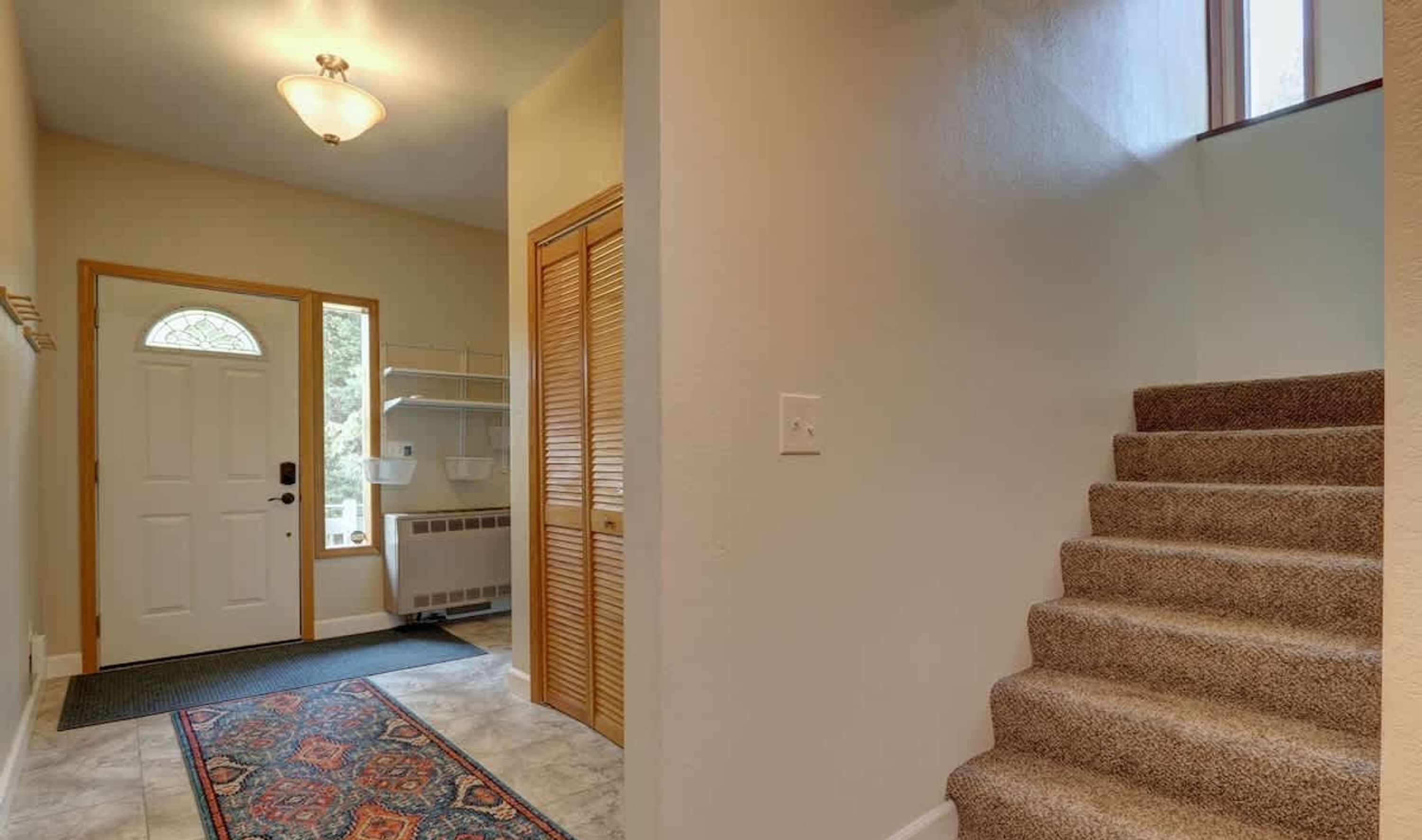 A hallway with a carpeted staircase, a door with a window, and a radiator.